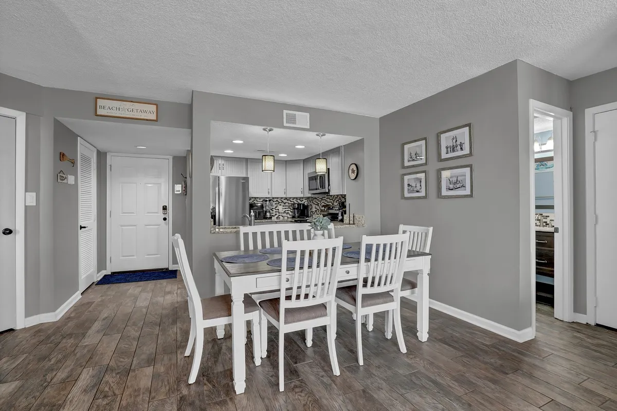 A welcoming dining area with a large table, stylish decor, and the kitchen entrance in view. Decorative wall art and soft ambient lighting suggest a space designed for family meals and social gatherings.