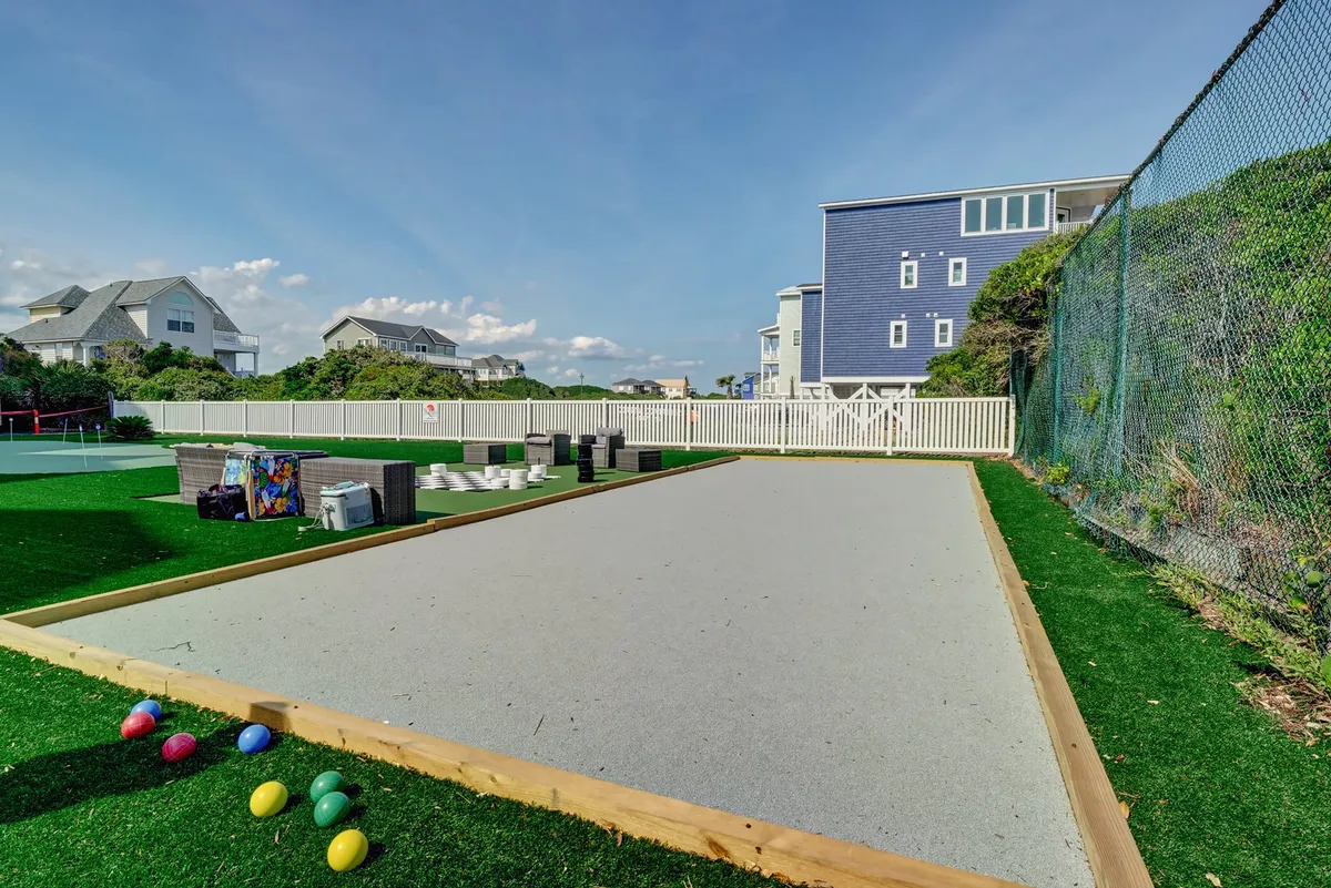 This exterior photo features a bocce ball court with colorful bocce balls scattered on lush green grass. The court is surrounded by nearby houses and includes a convenient sitting area for spectators or players to relax between games, creating a lively yet laid-back atmosphere.