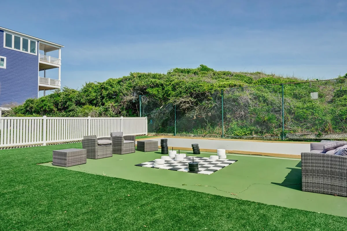 An outdoor scene showcasing a large life-size chess set anchored by a comfortable seating area, with vibrant greenery framing the background. The area invites guests to both play and relax outdoors, emphasizing leisure and friendly rivalry.
