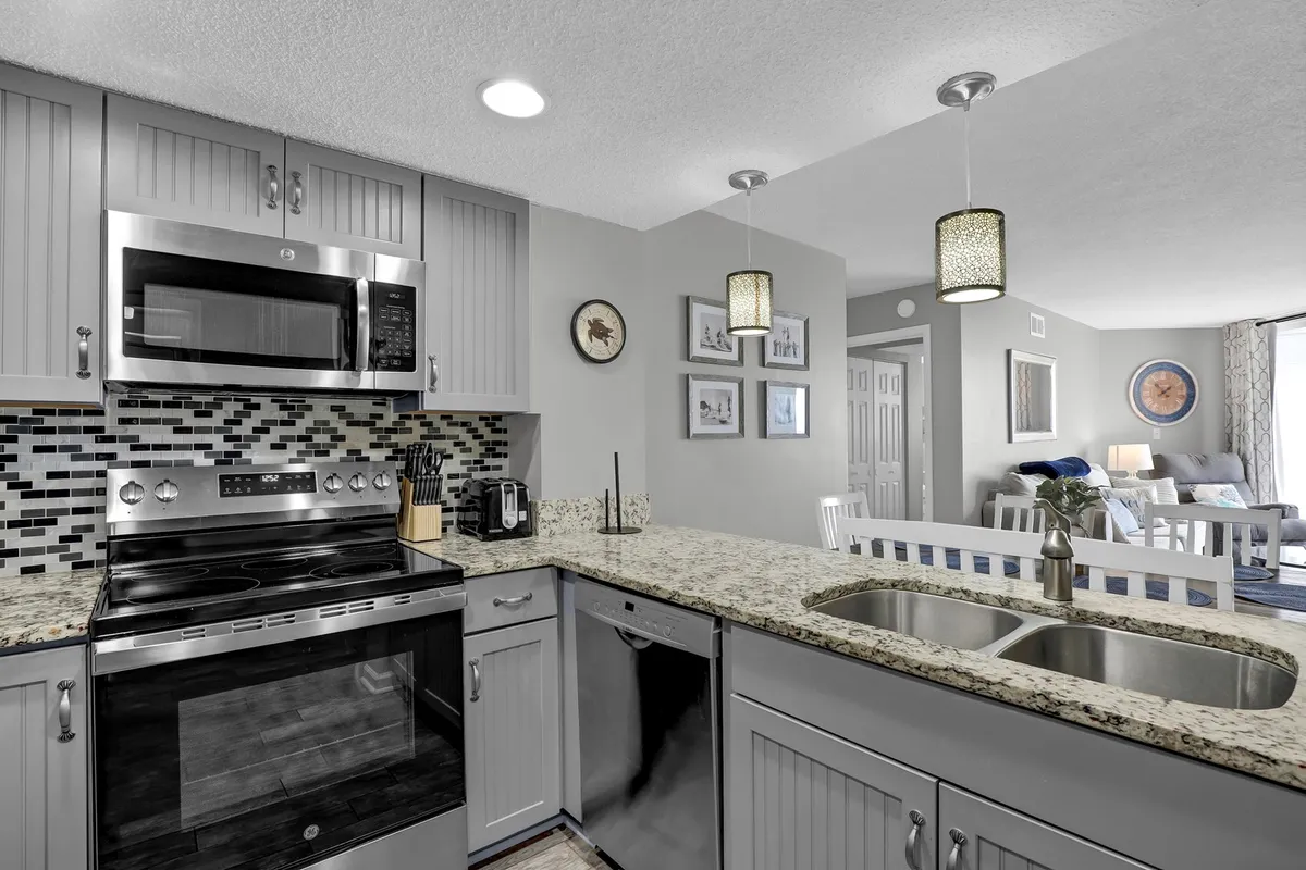 A welcoming, stylish kitchen featuring stainless steel appliances, granite countertops, a mosaic tile backsplash, and pendant lighting. Framed artwork on the walls and tasteful decor create a warm and inviting space ideal for cooking and entertaining.
