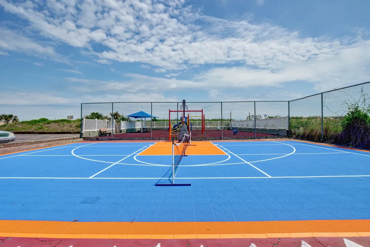 A colorful outdoor area featuring a basketball court, tennis net, and playground equipment. The layout makes it clear that this is a space for sports, play, and family activities, encouraging both competitive games and children's recreation.