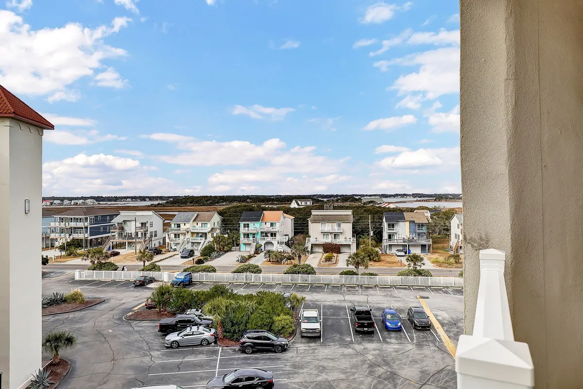 A view of colorful beach houses under an open sky, with a paved parking lot in front. The scene invites leisurely walks and exploration, evoking a relaxed coastal ambiance and the charm of the surrounding neighborhood.