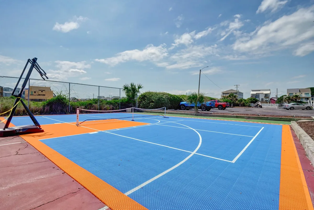 An exterior view of a multi-functional sports court with a basketball hoop and tennis net, set against a bright, energetic backdrop. The court is ideal for active pursuits and outdoor exercise.