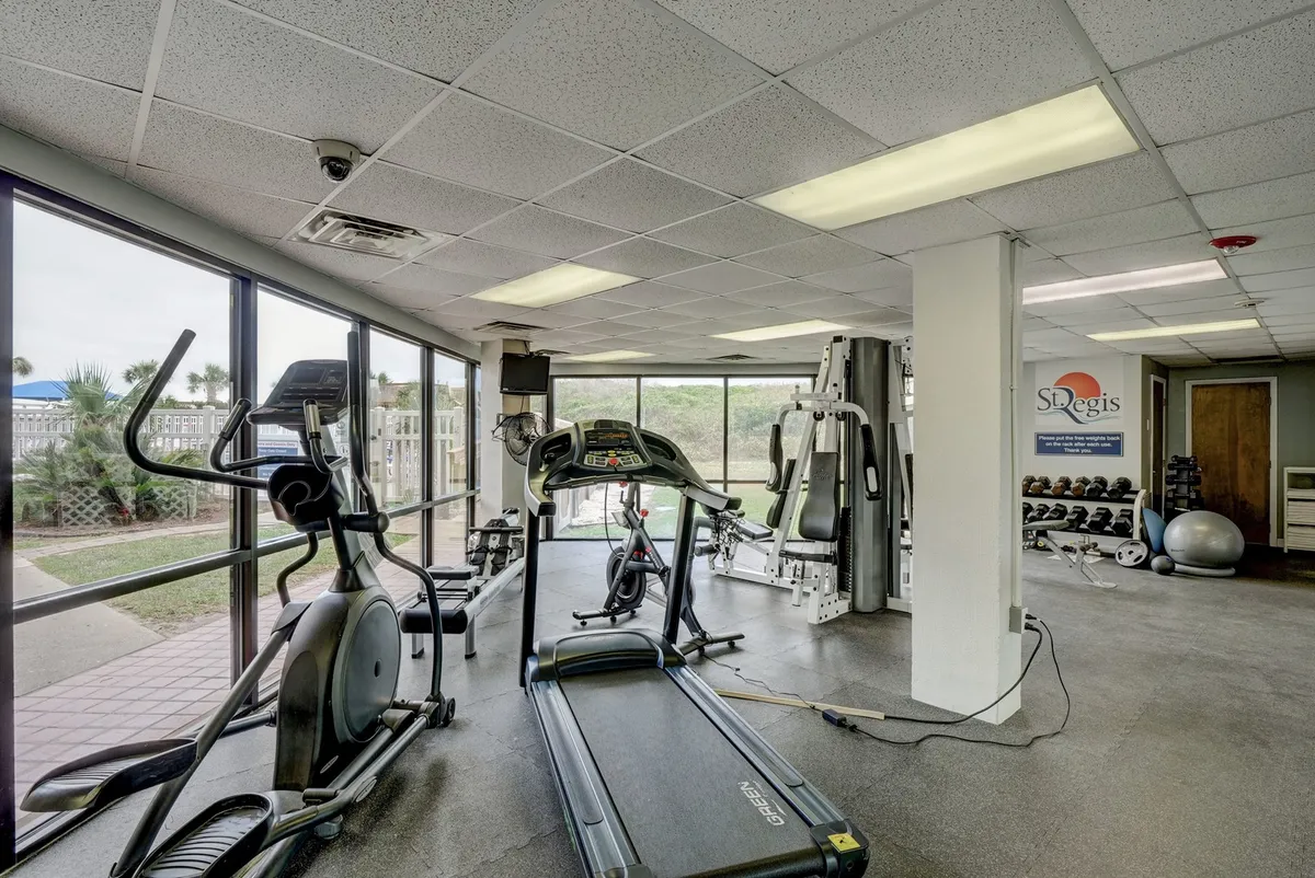 A well-equipped fitness center featuring treadmills, elliptical machines, and weight training equipment, with ample natural light filtering in. The space looks modern and energetic, ideal for staying active and maintaining wellness routines.