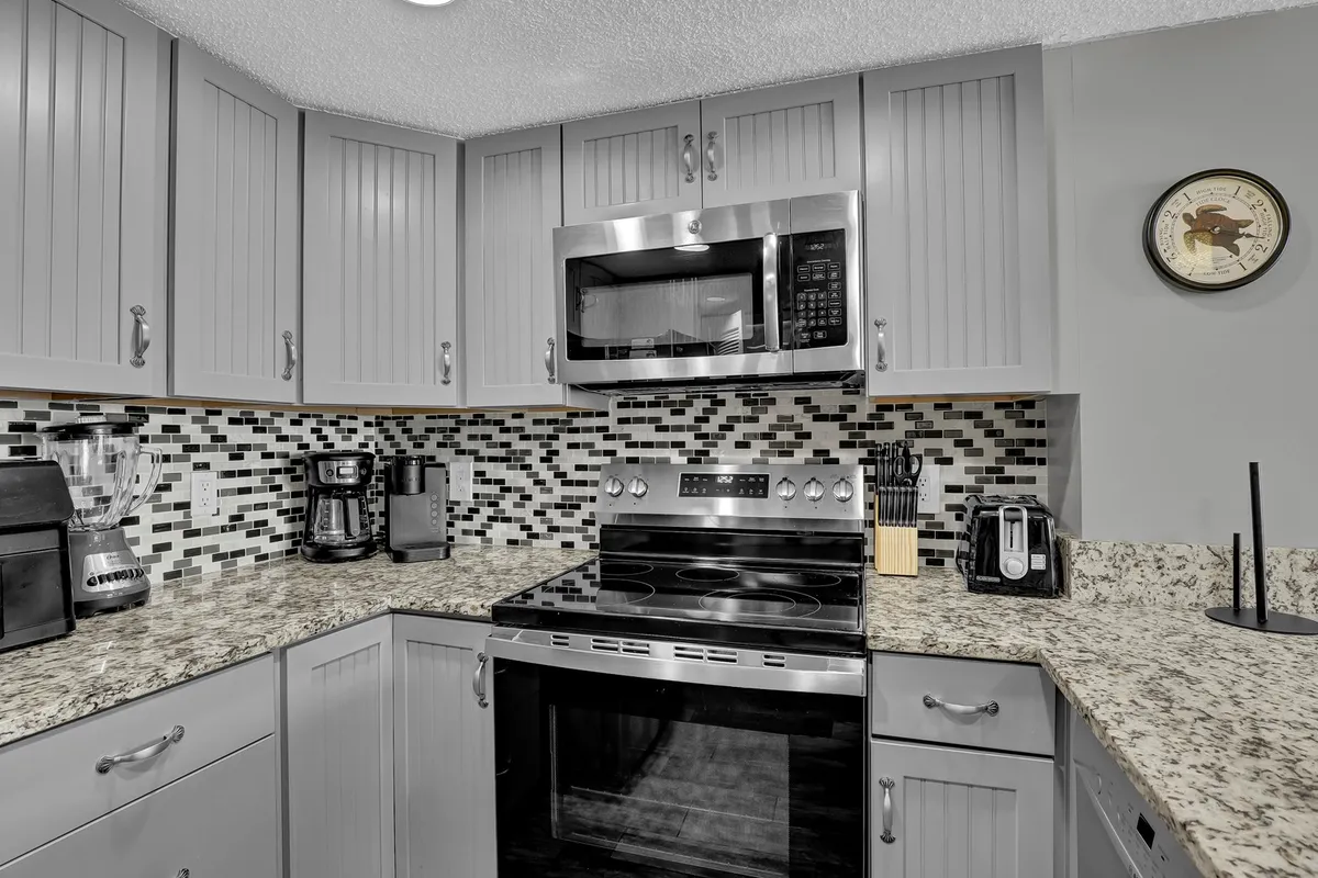 A functional, contemporary kitchen with a prominent granite countertop, stainless steel appliances, and a stylish mosaic backsplash. A coffee maker and ample workspace signal both everyday convenience and readiness for entertaining guests.
