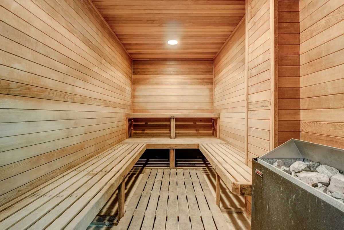 A cozy sauna interior featuring wooden benches and a stone heater creates a tranquil wellness retreat, ideal for relaxation and recovery after a workout.